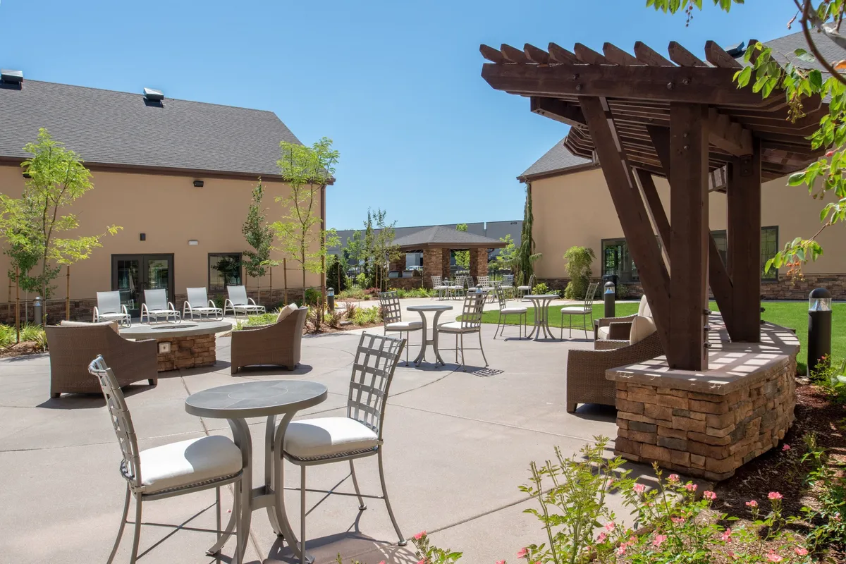 A welcoming outdoor seating area with a pergola surrounded by lush greenery, furnished with tables and chairs. The setting is casual, making it suitable for family gatherings, outdoor dining, or picnics after a day exploring local attractions.