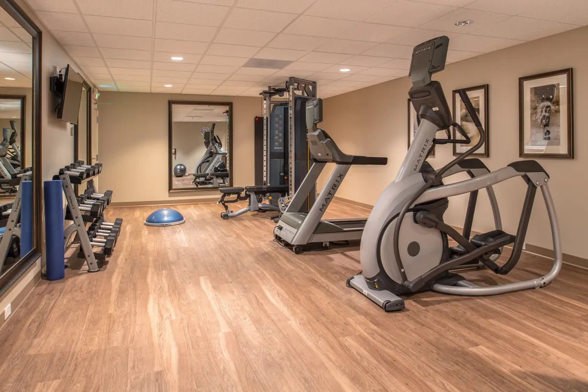 A bright and well-equipped fitness center with an elliptical machine, weight bench, exercise balls, and a large mirror. The space is designed for both individual workouts and group fitness, showcasing a motivational and energetic environment.