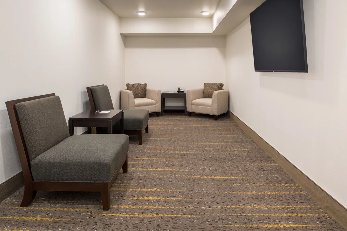 A comfortable nook featuring two upholstered armchairs around a small wooden table and a wall-mounted television, perfect for intimate conversations or enjoying a quiet moment together.