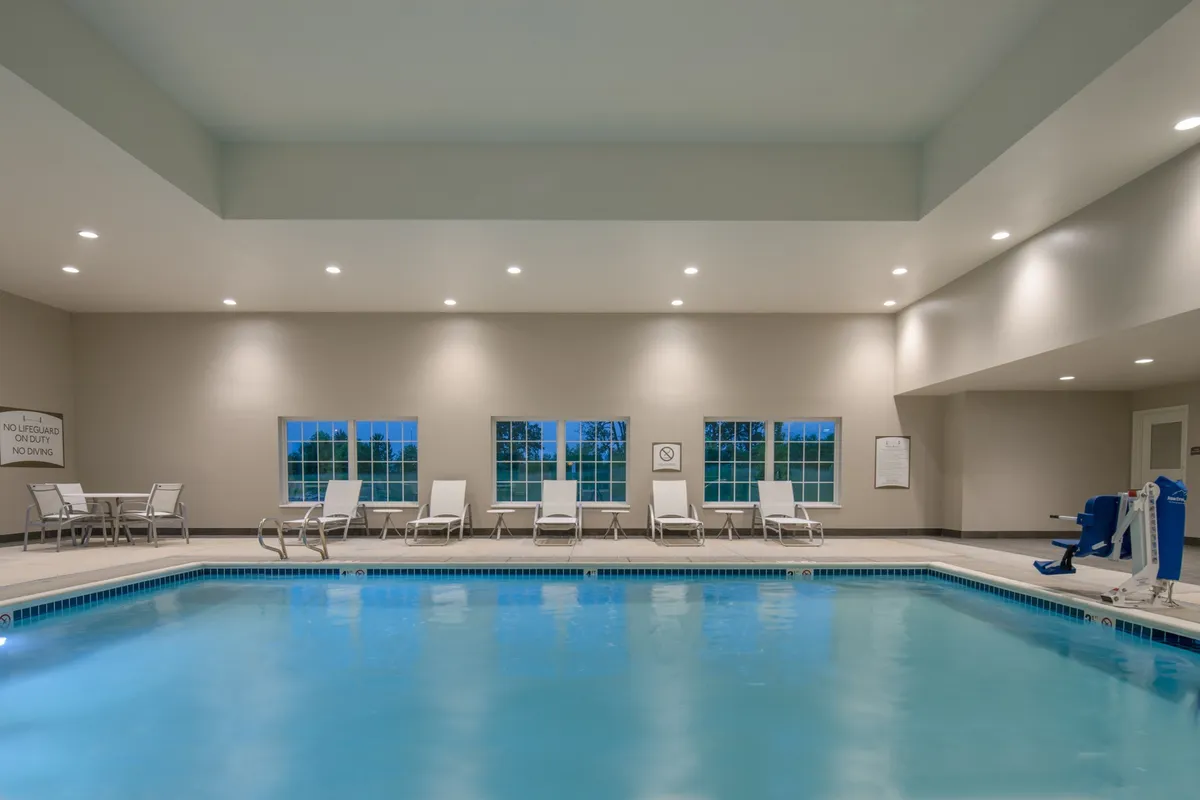 A tranquil indoor swimming pool area featuring clear blue water, several lounge chairs arranged along the poolside, and expansive windows letting in natural light. The atmosphere is inviting, perfectly suited for relaxation or socializing after a busy day.